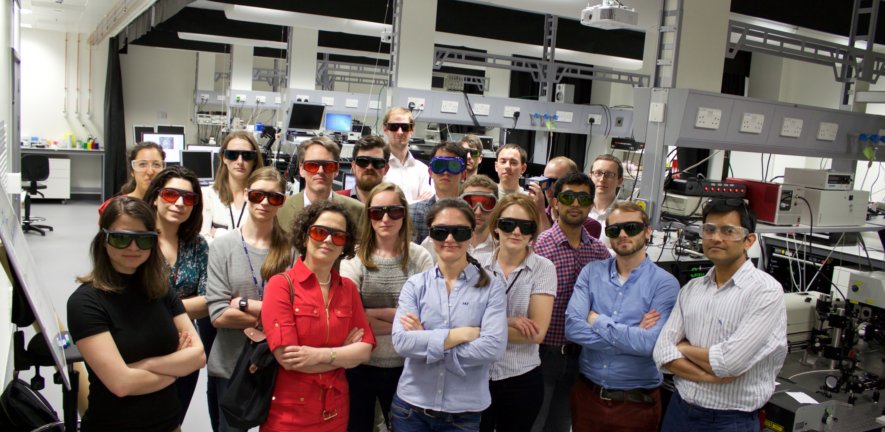 Sporting a varied assortment of protective eyewear, the Laser Analytics Group, Molecular Neuroscience Group, and Quantitative Imaging Group pose for a picture during the opening ceremony of our new laboratory space in West Cambridge. 